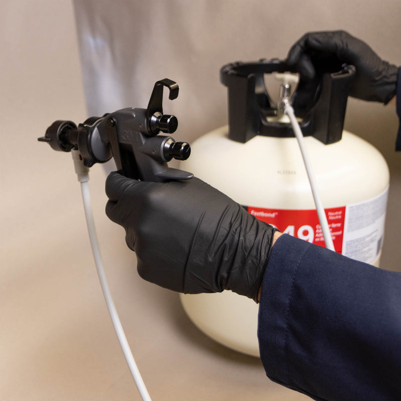 Technician holding 3M Water-Based Spray Adhesive Gun attached to Fastbond 1049 cylinder during setup.
