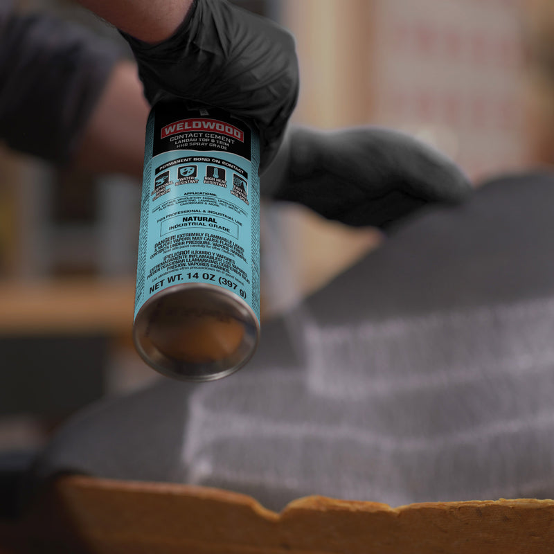 Close-up of DAP Weldwood Landau Top & Trim spray adhesive can being applied to upholstery in workshop setting