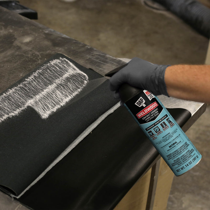 Spraying DAP Weldwood HHR Contact Adhesive onto layered black foam and vinyl for upholstery bonding