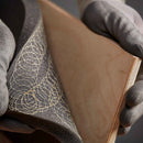 Close-up view of hot melt adhesive sprayed between foam and wood, showing bonded materials after application.