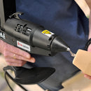 A controlled bead of hot melt adhesive flows from the nozzle of the Power Adhesives Tec 7100 glue gun onto a wood component.